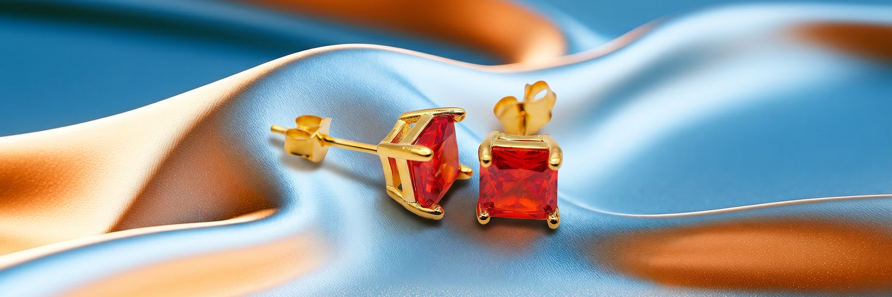 Goldfarbene Ohrstecker mit rotem Zirkonia auf blau-orangem Stoff