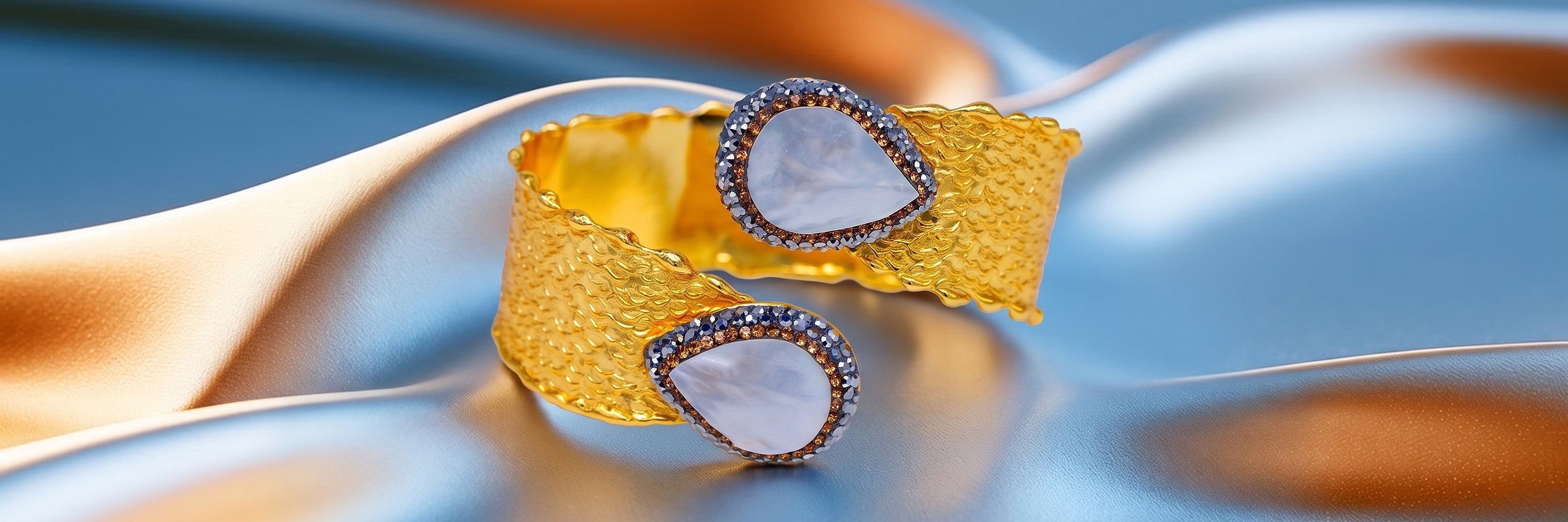 Goldfarbener Armreif in Perlmutt-Optik mit Kristallrand auf blau-orangem Stoff