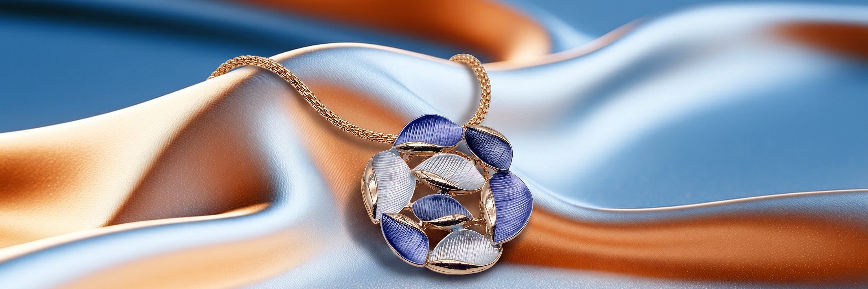 Goldfarbene Halskette mit blau-weissem Blätter-Anhänger auf blau-orangem Stoff.
