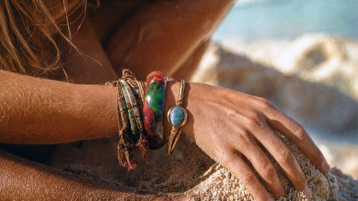 Nahaufnahme einer Frau, die einen Stack aus verschiedenen goldfarbenen, perlenbesetzten und Gliederketten-Armbändern am Handgelenk trägt.